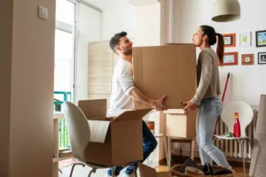 Couple carrying moving boxes inside apartment