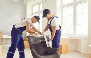 Movers wrapping an armchair with protective plastic.