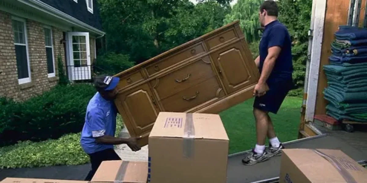 Two movers carrying a wooden dresser into a moving truck.